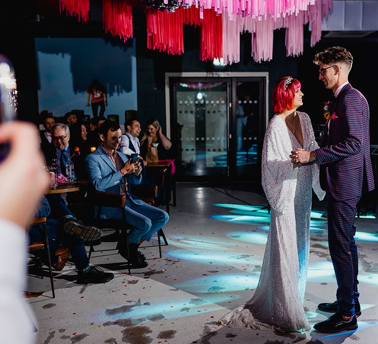 Bride in sparkly wedding dress with pink hair dancing with the groom in purple checkered suit 