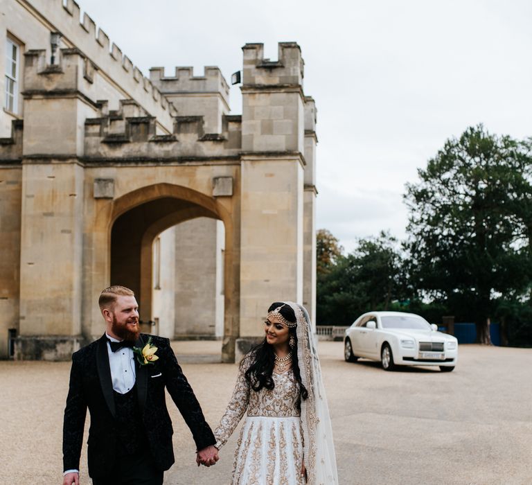 Indian bride in ivory and gold bespoke dress and groom in black tuxedo for fusion wedding