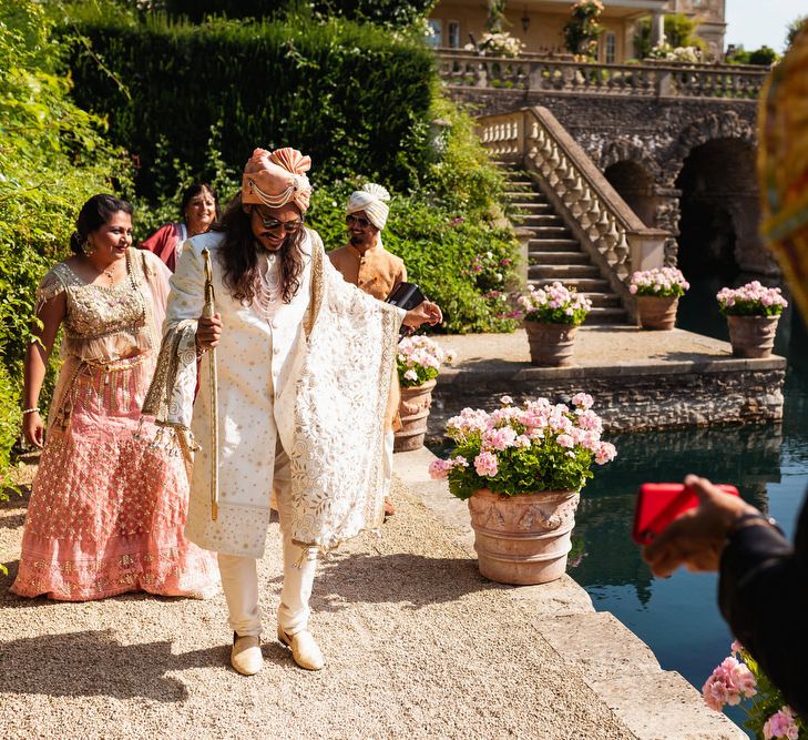 Groom in white and gold Indian outfit arriving for the intimate ceremony 