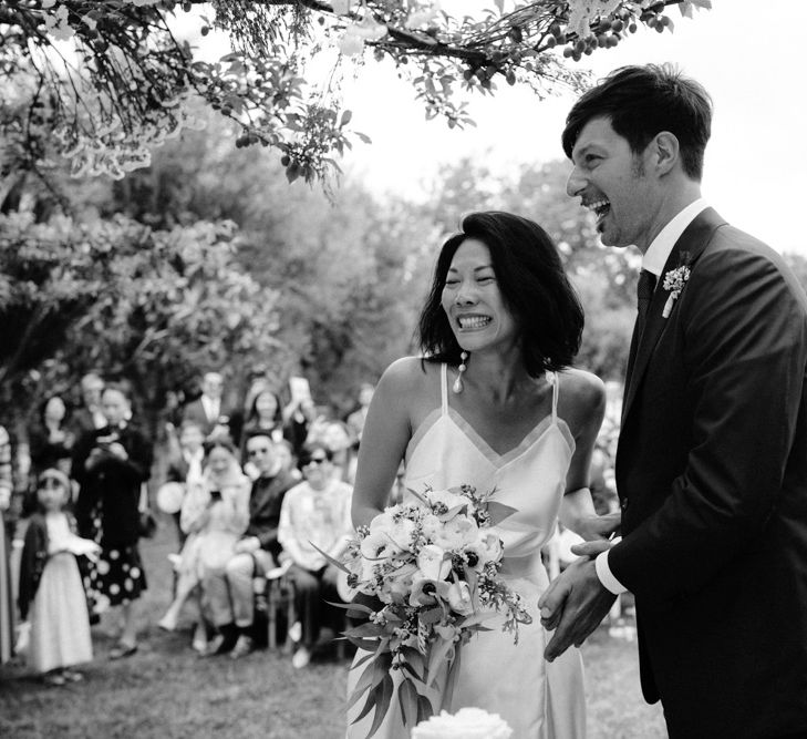 Black and white portrait of the bride and groom laughing during the outdoor wedding ceremony 