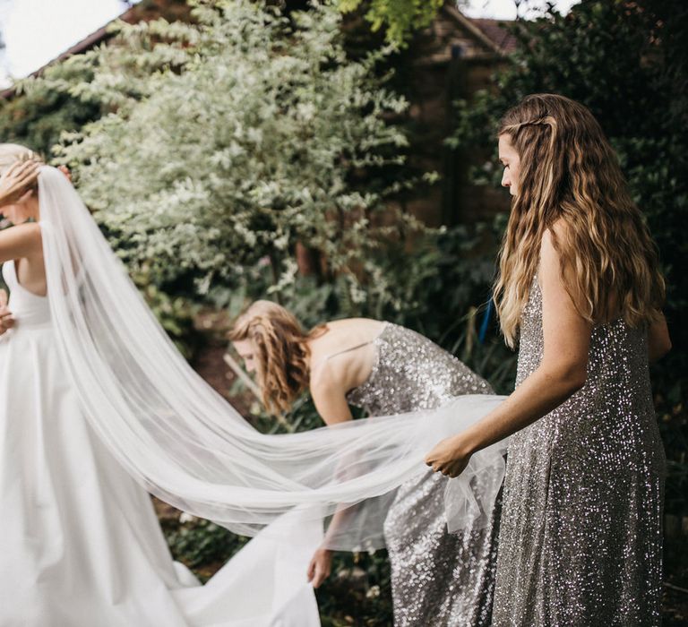 Bridesmaids in silver sequin midi dresses fanning out the brides train and veil 