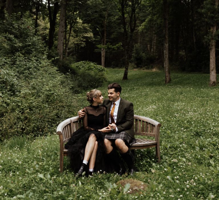 Bride & groom sit together on bench in the Scottish woodlands 