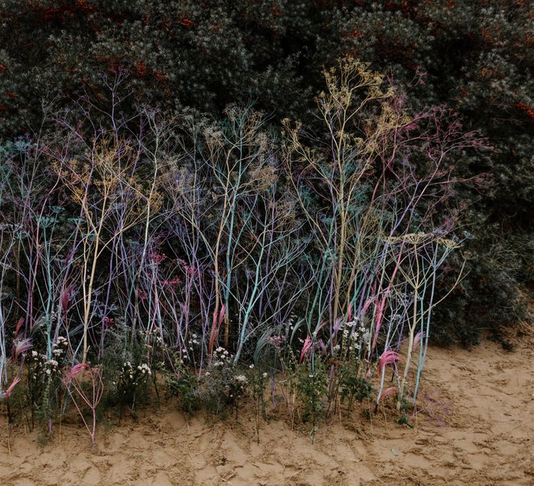 Colourful foliage stems plotted in the sand at a beach elopement 