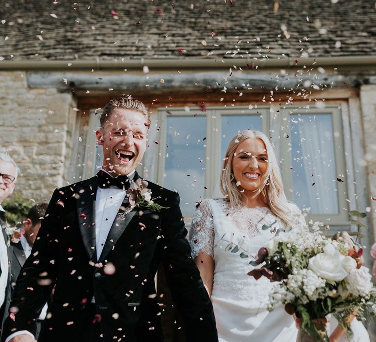 Bride in white Charlie Brear wedding dress and white Augusta Jones lace top and groom in black velvet Hugo Boss suit walk through confetti at Caswell House wedding