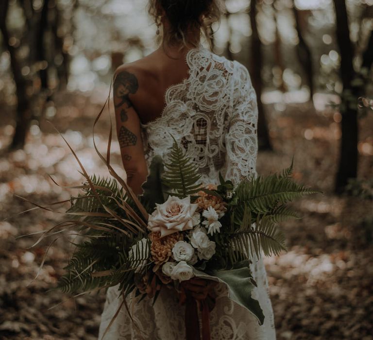 Bride in a boho lace wedding dress holding her bouquet behind her back 