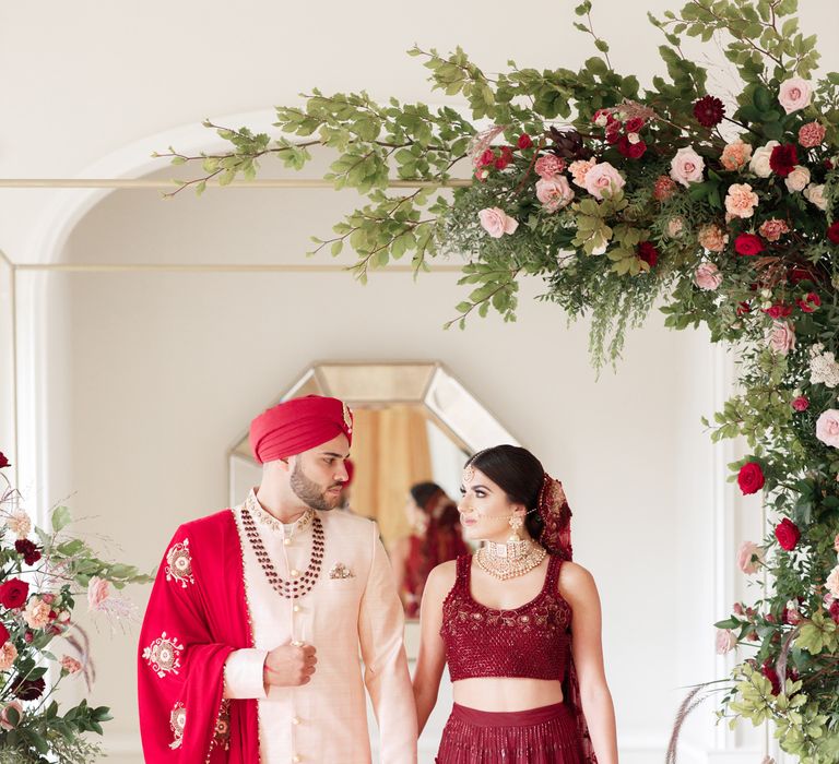 Bride & groom stand together under floral archway 