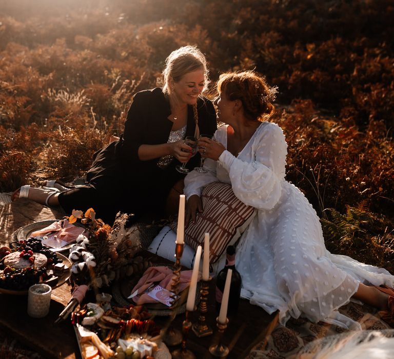 Same-sex couple cheers-ing at sunset over beach picnic