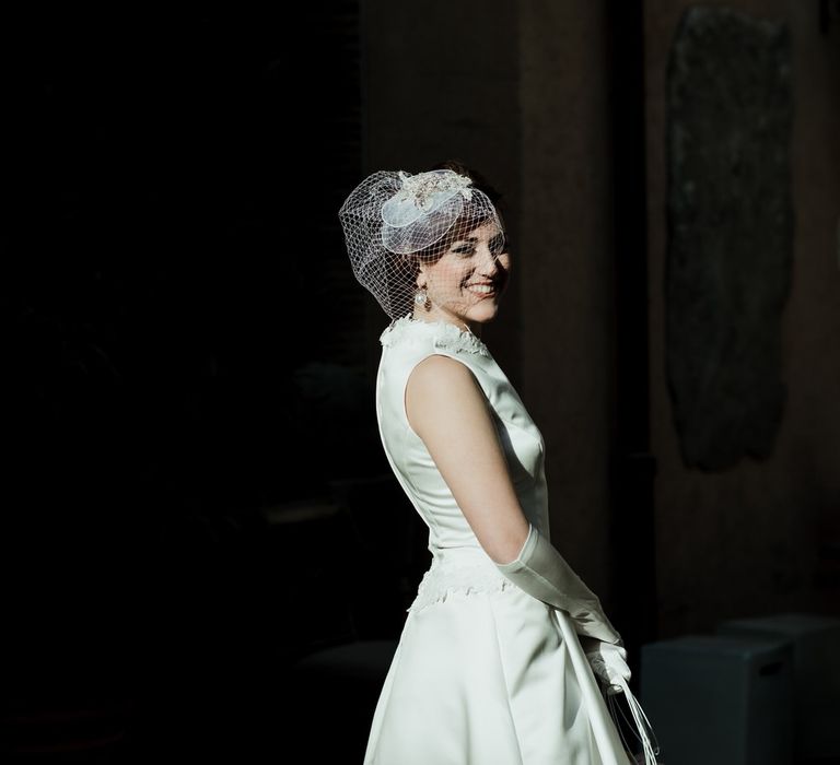 Bride wearing vintage style wedding dress, silk bridal gloves and vintage hat with short net veil detail