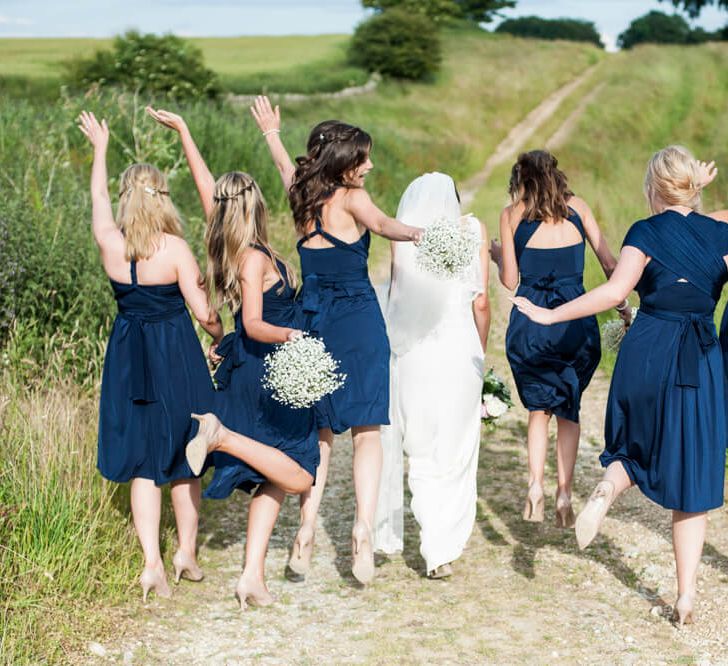 Bridesmaids in multiway navy blue knee length dresses holding gypsophila bouquets skipping through the countryside | Marks and Spencer Dresses | Eleanor Jane Photography