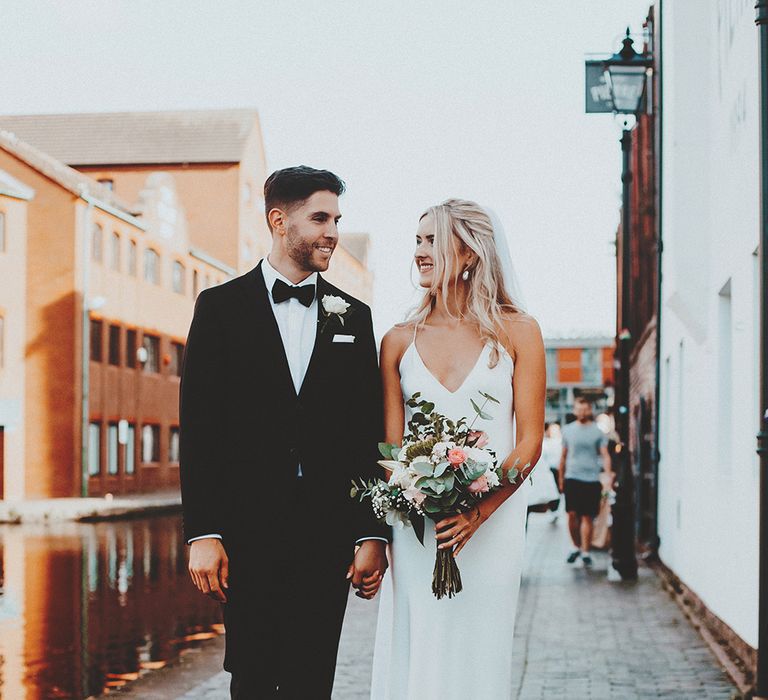 Groom in a tuxedo and bride in a slip wedding dress walking along the canal in Birmingham 