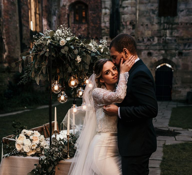 Intimate bride and groom portrait next to their intimate wedding reception table with festoon lights and foliage decor 