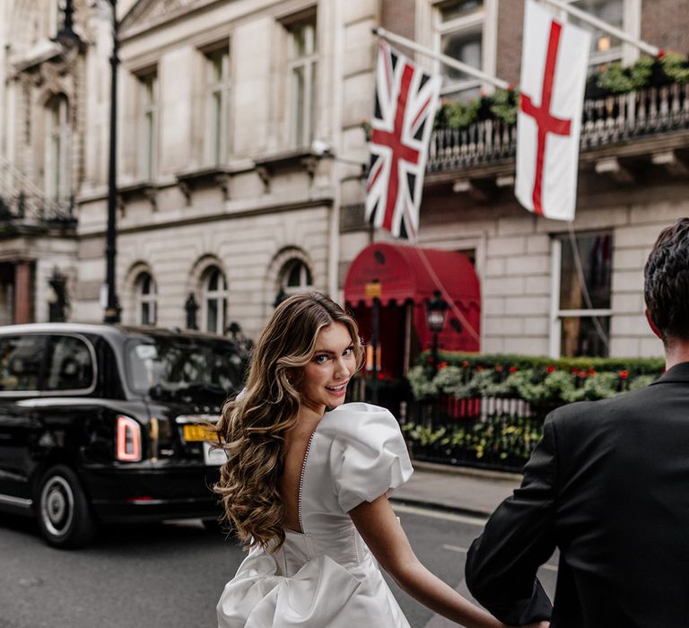 City bride in a short wedding dress with low back and bow detail with long curly hair and pink eyeshadow 