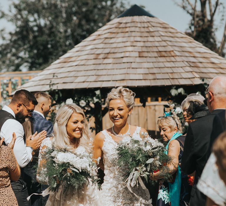 Two brides exit their outdoor wedding ceremony laughing. 