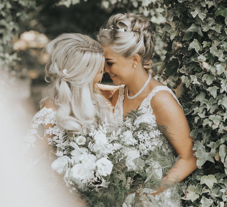 Two brides embrace under a canopy of flowers.