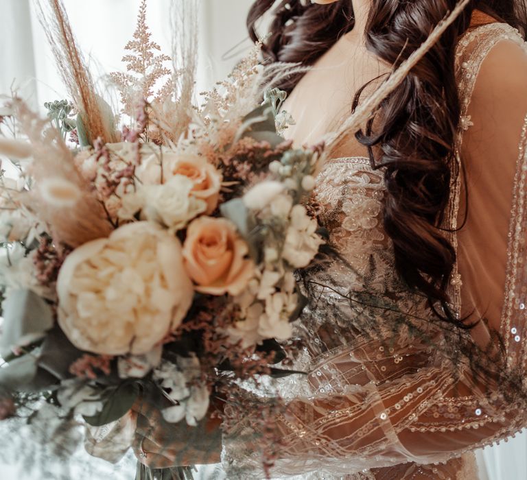 Bride holds floral bouquet filled with roses and green foliage on her wedding day