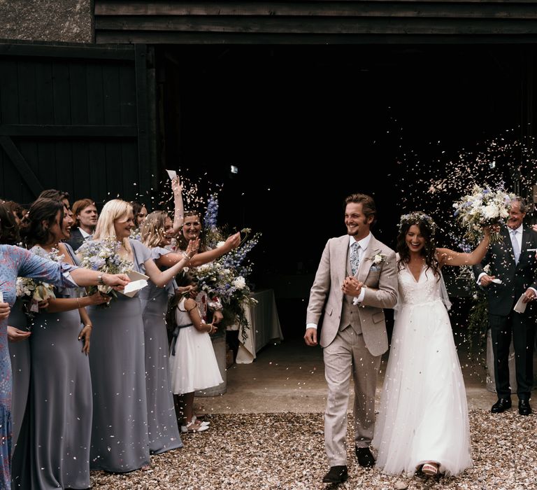 Bride & groom leave rustic barn after wedding ceremony as wedding party throw confetti around them