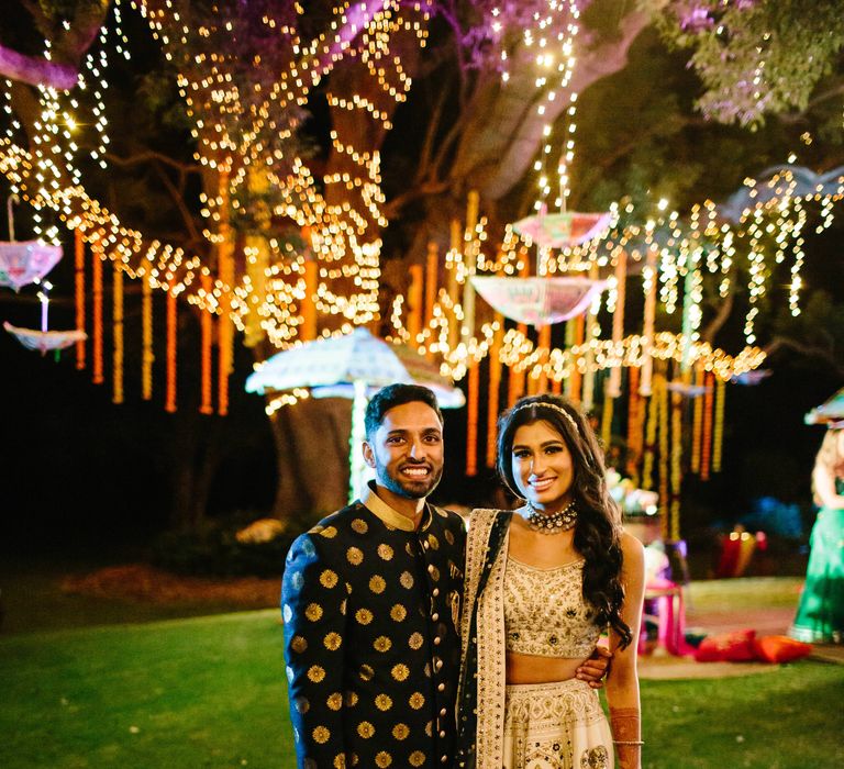 Bride & groom stand outdoors as beautiful bright lights can be seen within the background