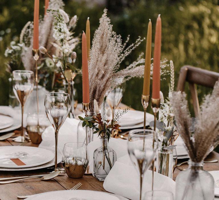 Natural wedding table decor with orange taper candles, gold candlesticks and dried grass stems in vases 