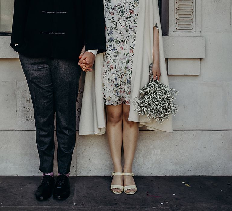 Stylish bride and groom in tampered trousers and a short wedding dress holding a gypsophila wedding bouquet