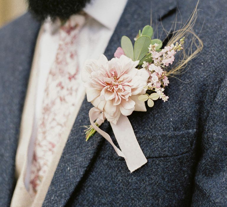 Groom in a blue wool suit with floral tie and pale pink dahlia buttonhole 