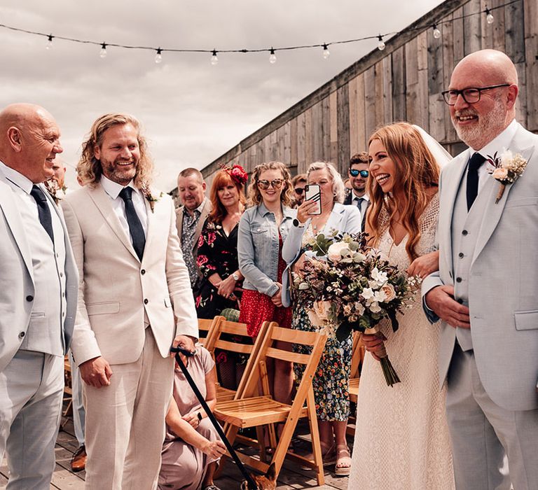 Bride greets her groom at the outdoor wedding ceremony holding artificial wedding bouquet