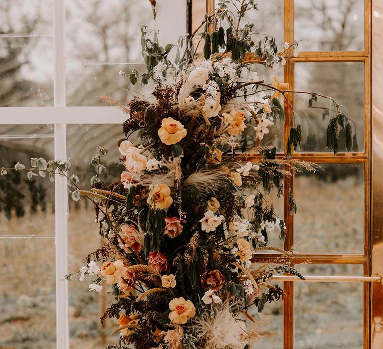 Vertical yellow and orange fresh flower and dried grass floral arrangement decorating the altar at The Gooseberry House