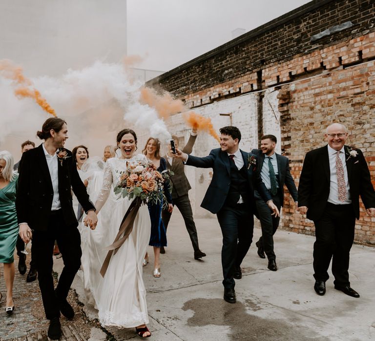 Intimate Clapton Country Club wedding with wedding guests holding smoke bombs in the courtyard behind the bride and groom 