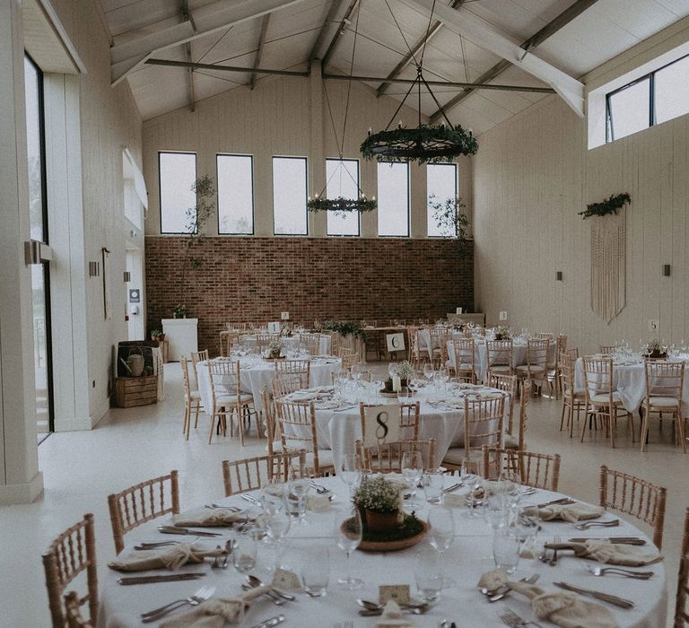 Round tables with white tablecloth and bamboo chairs in barn at East Afton Farmhouse for wedding breakfast with macrame wedding decor 