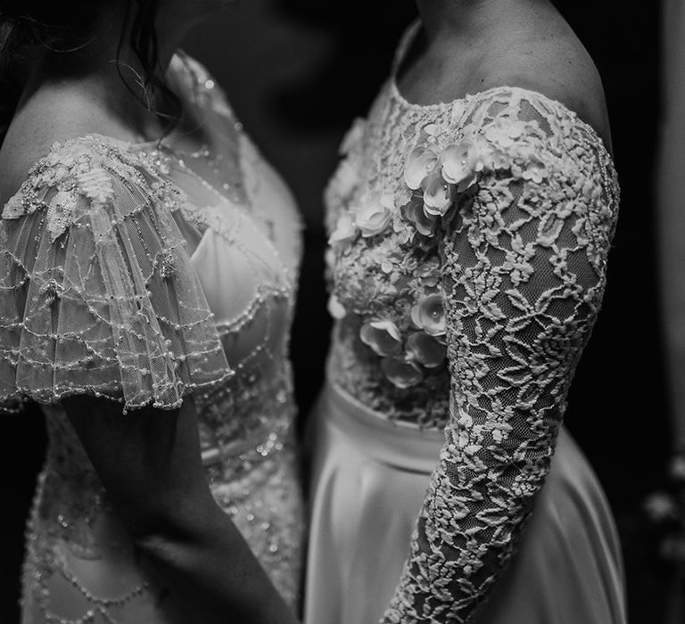 Black and white portrait of the detail on the brides wedding dresses with embellished cap sleeves and lace, appliqué long sleeves 