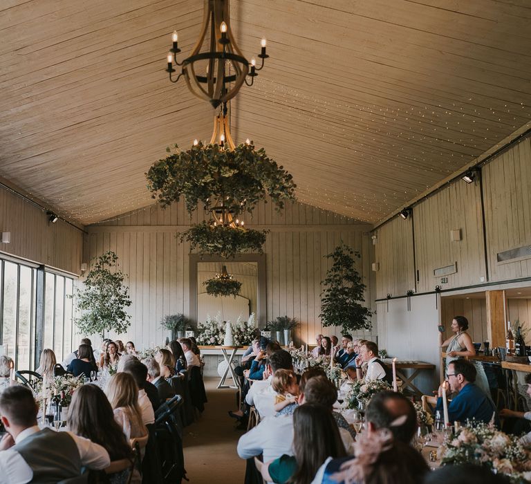 Interior of barn wedding breakfast with long white tables, mixed florals and lit dinner candles at Primrose Hill Farm wedding