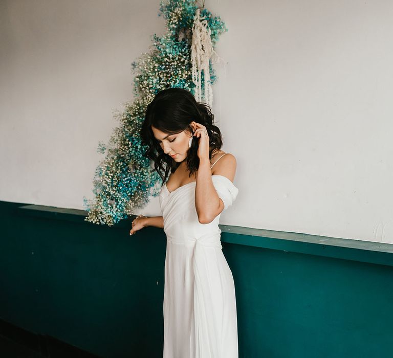 Bride in a cold shoulder wedding dress standing next to a white a teal gypsophila flower cloud 