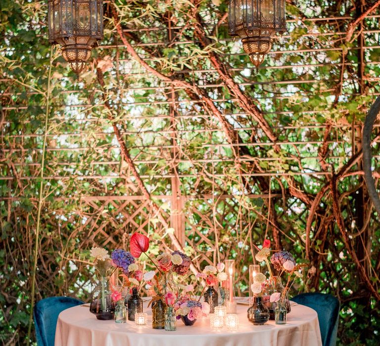 Round table complete with white tablecloth and bright florals set within different vases