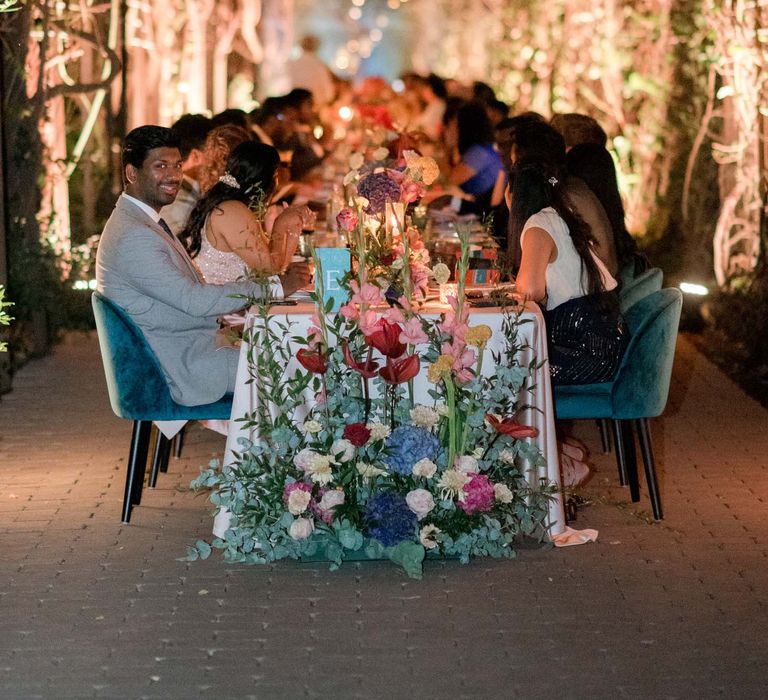 Beautifully lit pergola with hanging lanterns and colourful tablescape complete with pastel floral installation at the bottom