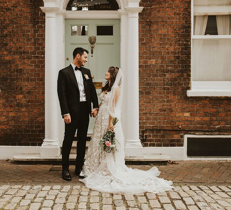 Bride looks up at her groom on her wedding day as they stand in front of pastel green door 