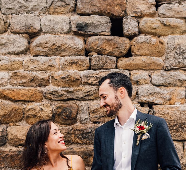 Bride & groom laugh in front of brick wall on their wedding day