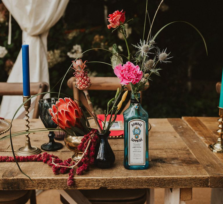 Gin bottles and vessels filled with colourful flower stems wedding table decor 