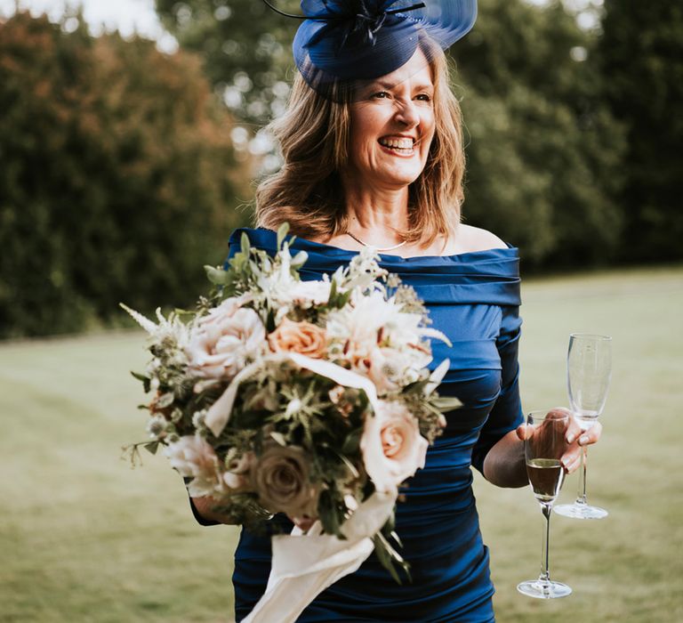 Mother of the bride in a navy blue strapless dress and fascinator holding the romantic wedding bouquet tied with ribbon 