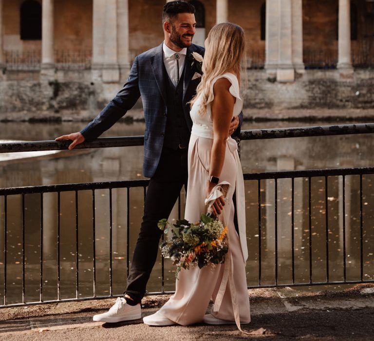 Intimate elopement in Bath with bride in a white and pink jumpsuit and groom in a navy suit and shoelace tie 