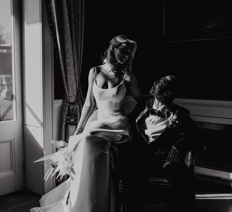 Black and white portrait of a bride sitting on her partners lap in a tuxedo at Hodsock Priory wedding venue 