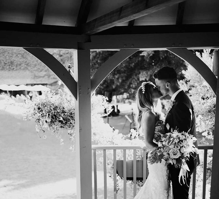 Bride in floral lace wedding dress with sheer train kisses groom in dark suit at Cooling Castle wedding venue