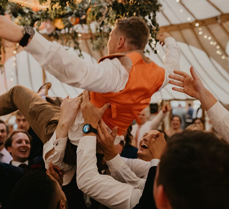 Groomsmen lift up the groom during the wedding reception