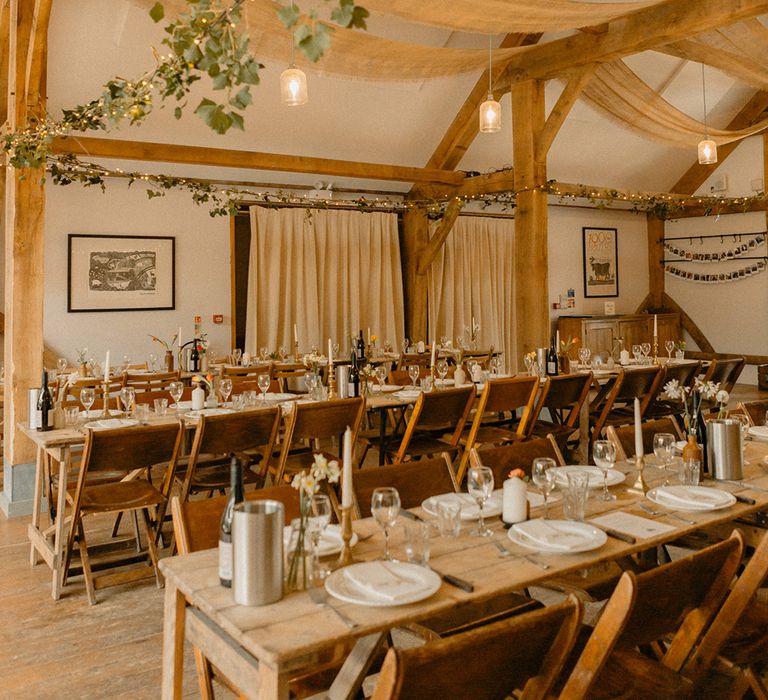 Rustic wooden banquet tables with brown chairs with decorative greenery, fairy lights and polaroids