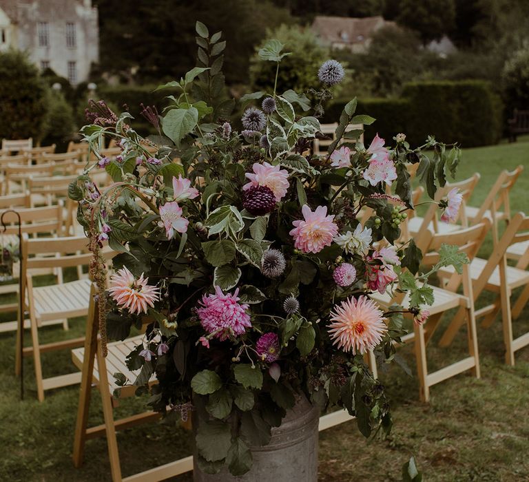 Pink and purple wedding flowers in vintage milk churns including dahlias and thistle 