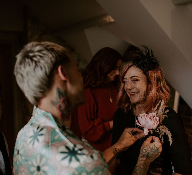 Groom puts floral buttonhole on mother on the morning of his wedding day