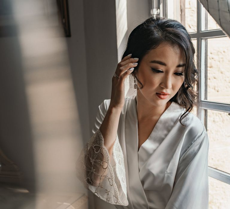 Bride wears short silk dressing gown complete with lace sleeves and natural makeup finished with peach lipstick and silver nails 