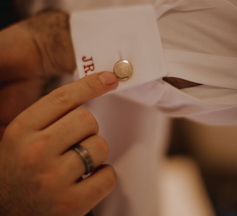 Groom wears personalised white shirt with stitched initials to cuff and engraved gold cufflinks 