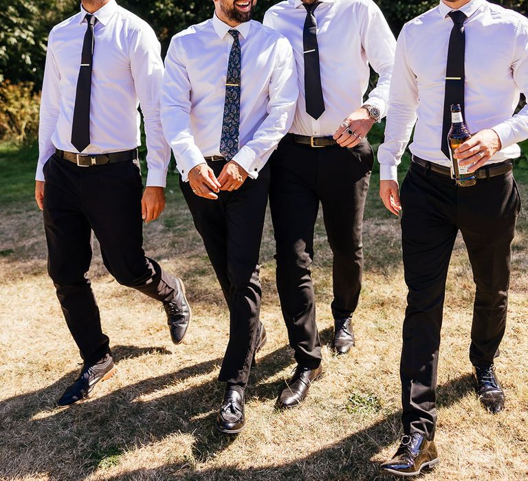 Groom walks with his groomsmen who wear white shirts and black ties with sunglasses outdoors 