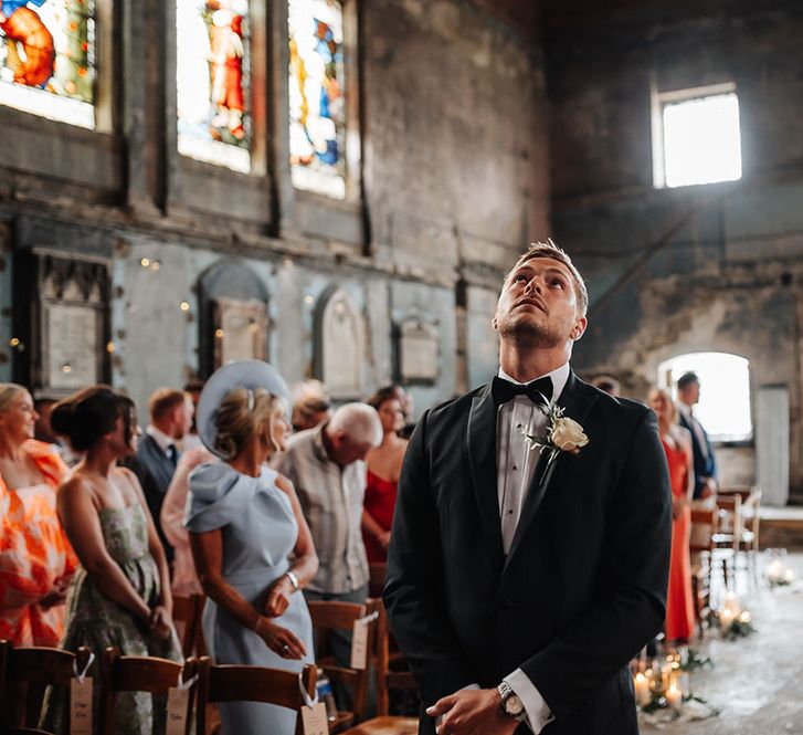 Groom wears black tie and floral buttonhole as he awaits his bride at The Asylum 