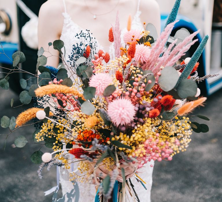 Bride with pixie haircut and embellished bridal crown holds dried floral bouquet filled with bright flowers 