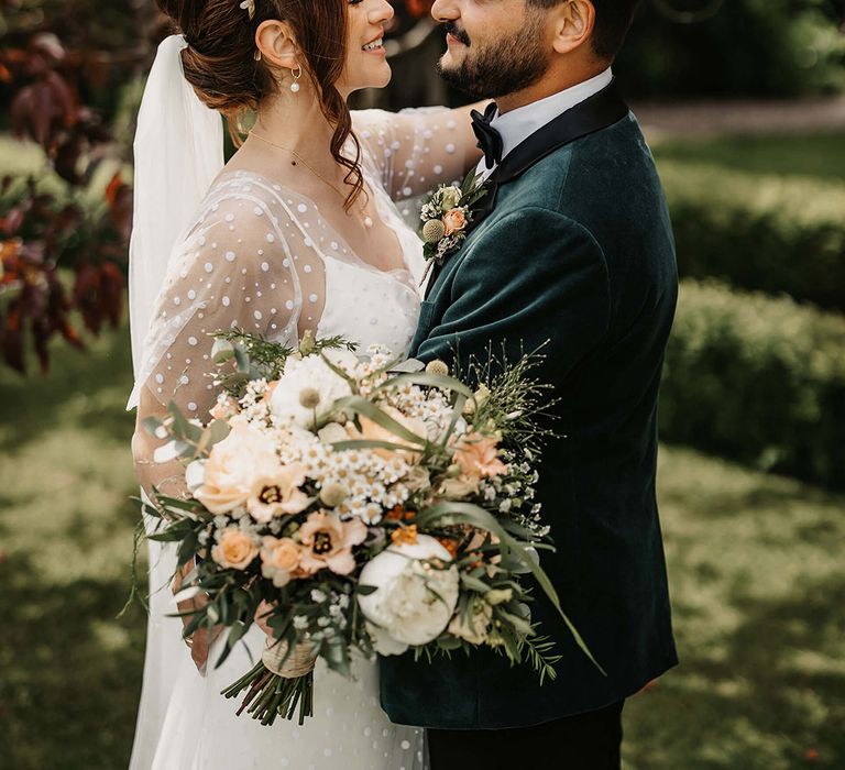 Bride in a quartz crystal crown gazes lovingly into the groom's eyes who wears a velvet custom suit jacket